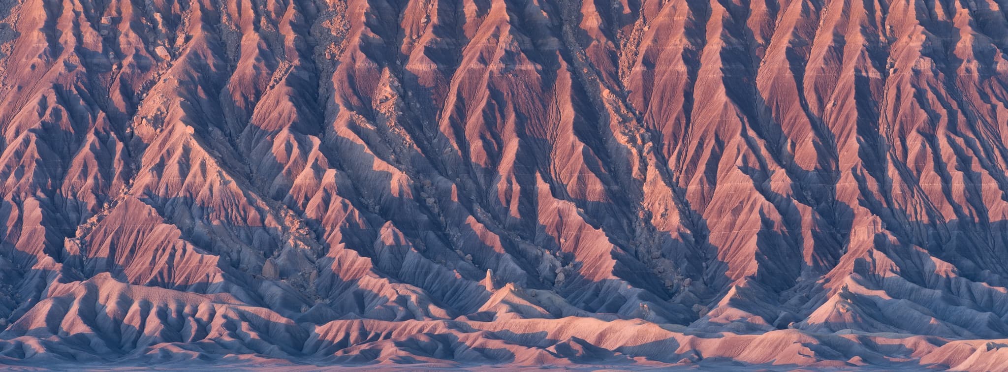 Factory Butte lit by the first light of a fall sunrise in Utah's badlands, the long shadows of morning cutting across the terrain. Photograph by Marty Quinn