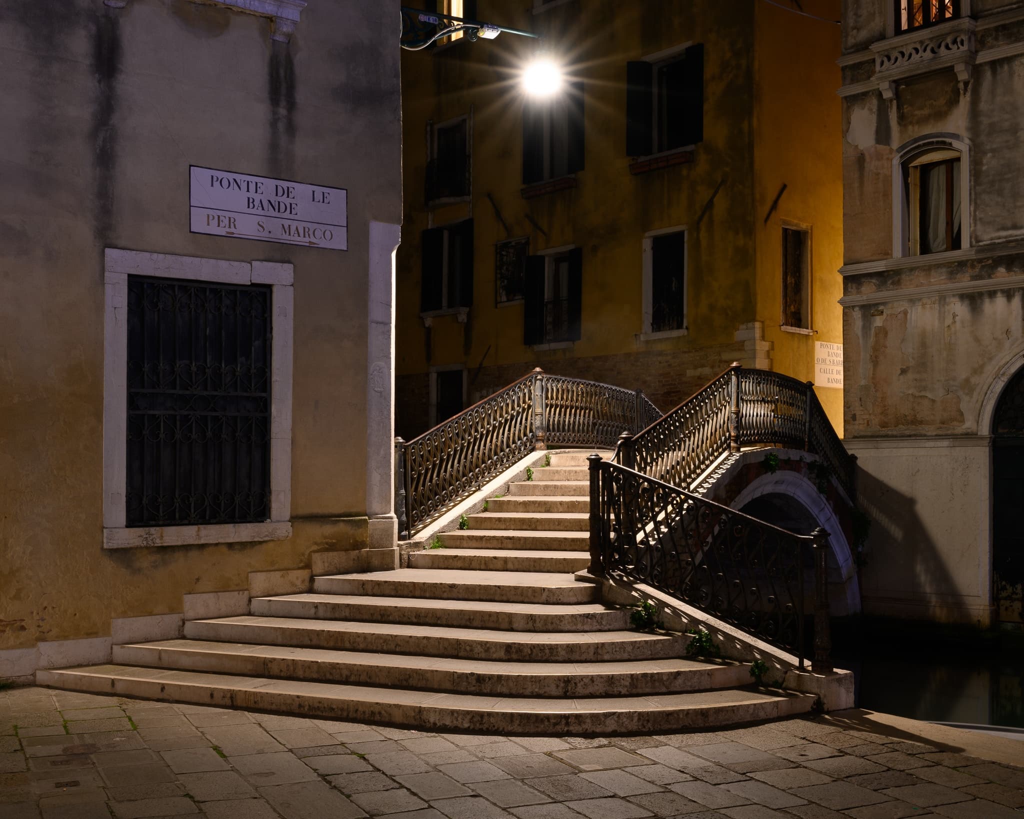 A stone staircase descends into a canal in Venice at night, the water moving slowly past old foundations, International. Photograph by Marty Quinn