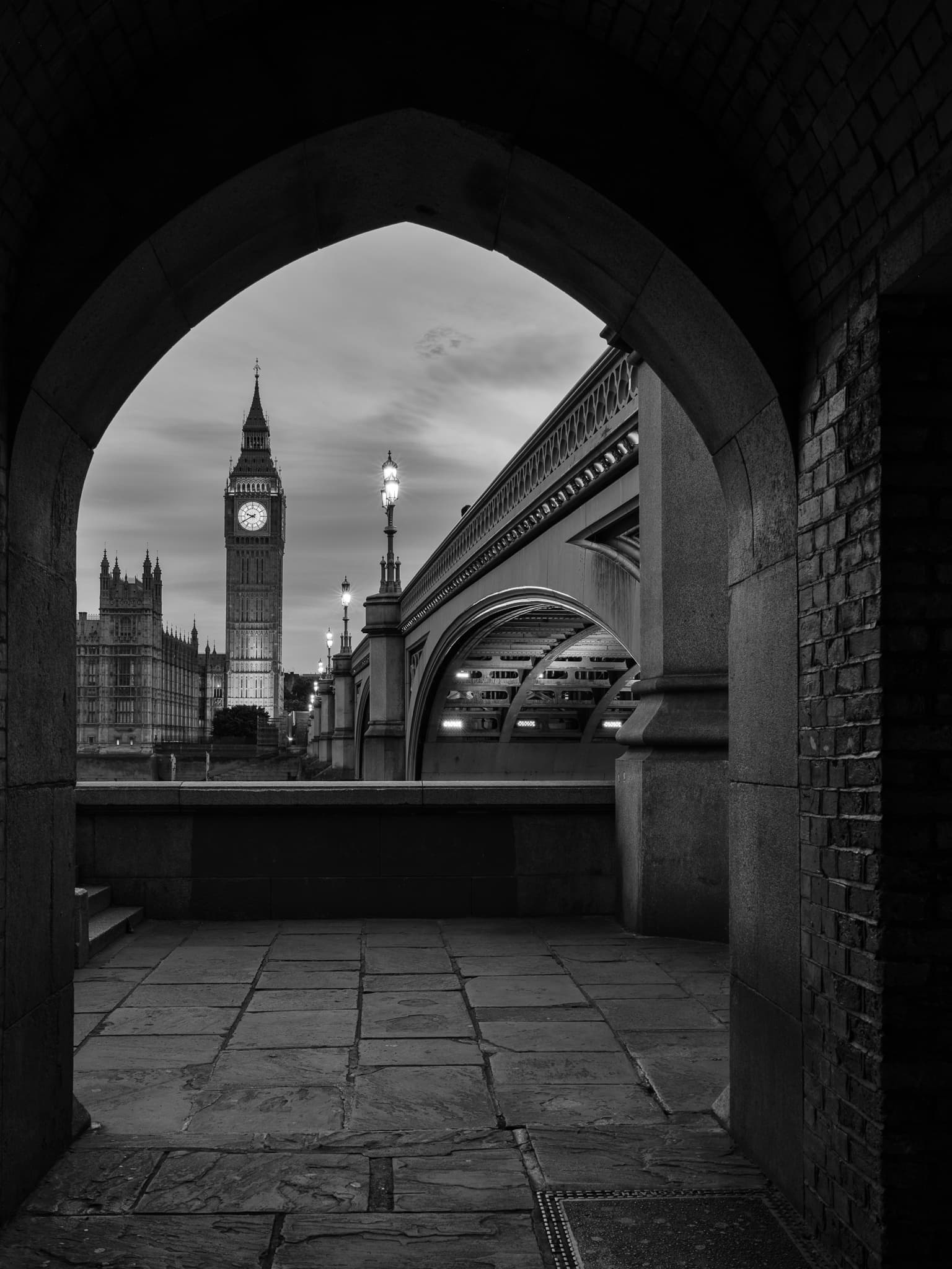 Big Ben and the Houses of Parliament framed through a stone archway near Westminster Bridge, London, at night, International. Photograph by Marty Quinn